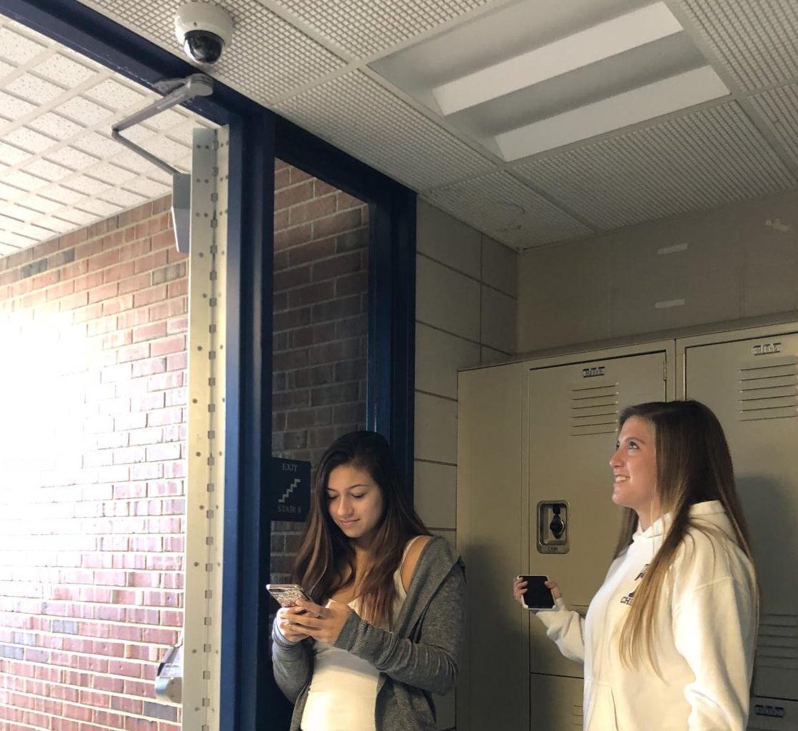 Students Lindsey Gardella, left, and Erin Drew stand beneath one of Tritons new cameras.