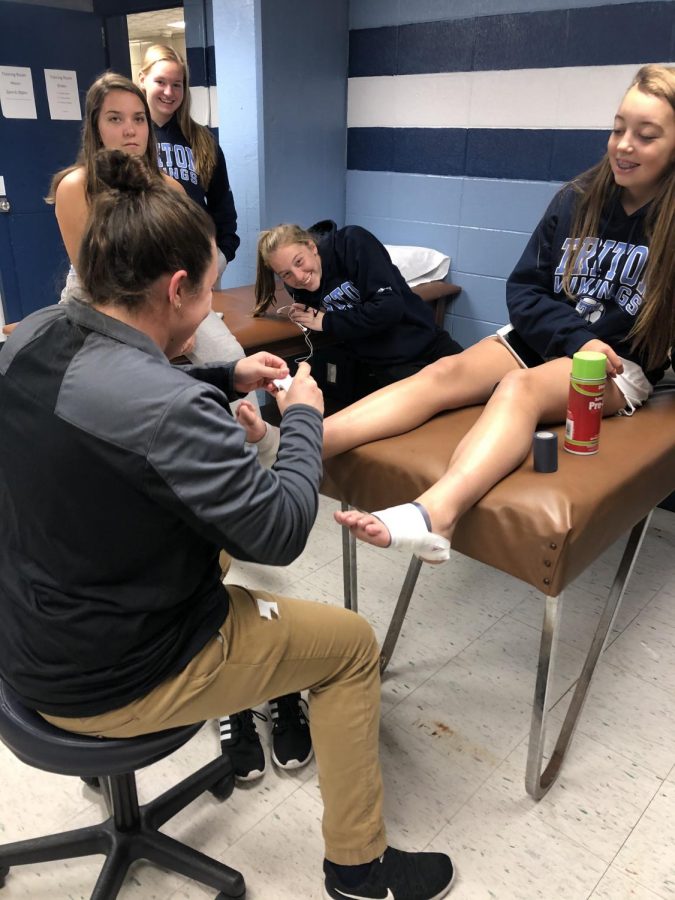 Macy Morrison taping a Triton athletes ankle before their practice 
