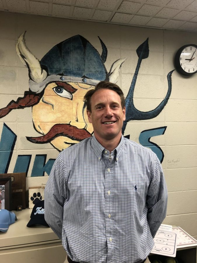 Tim Alberts standing in his office in front of Viking mascot.