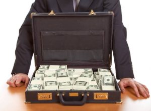 Business man standing next to open briefcase with money.